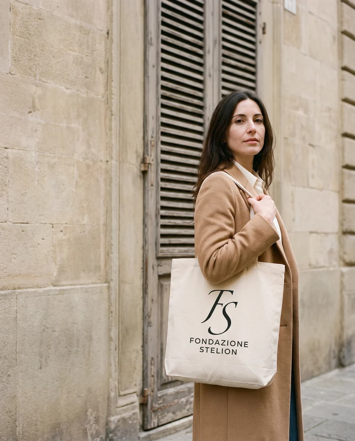 La borsa in tela di cotone grezzo portata a spalla, con il marchio stampato al centro.