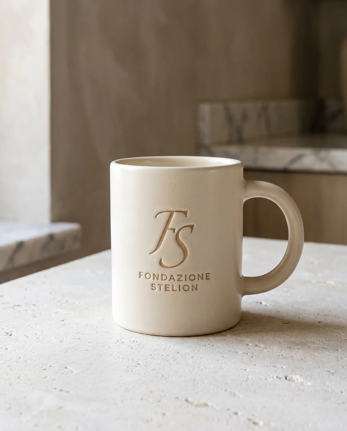 La tazza in gres a parete spessa, smalto opaco avorio, con il marchio inciso sul fianco.