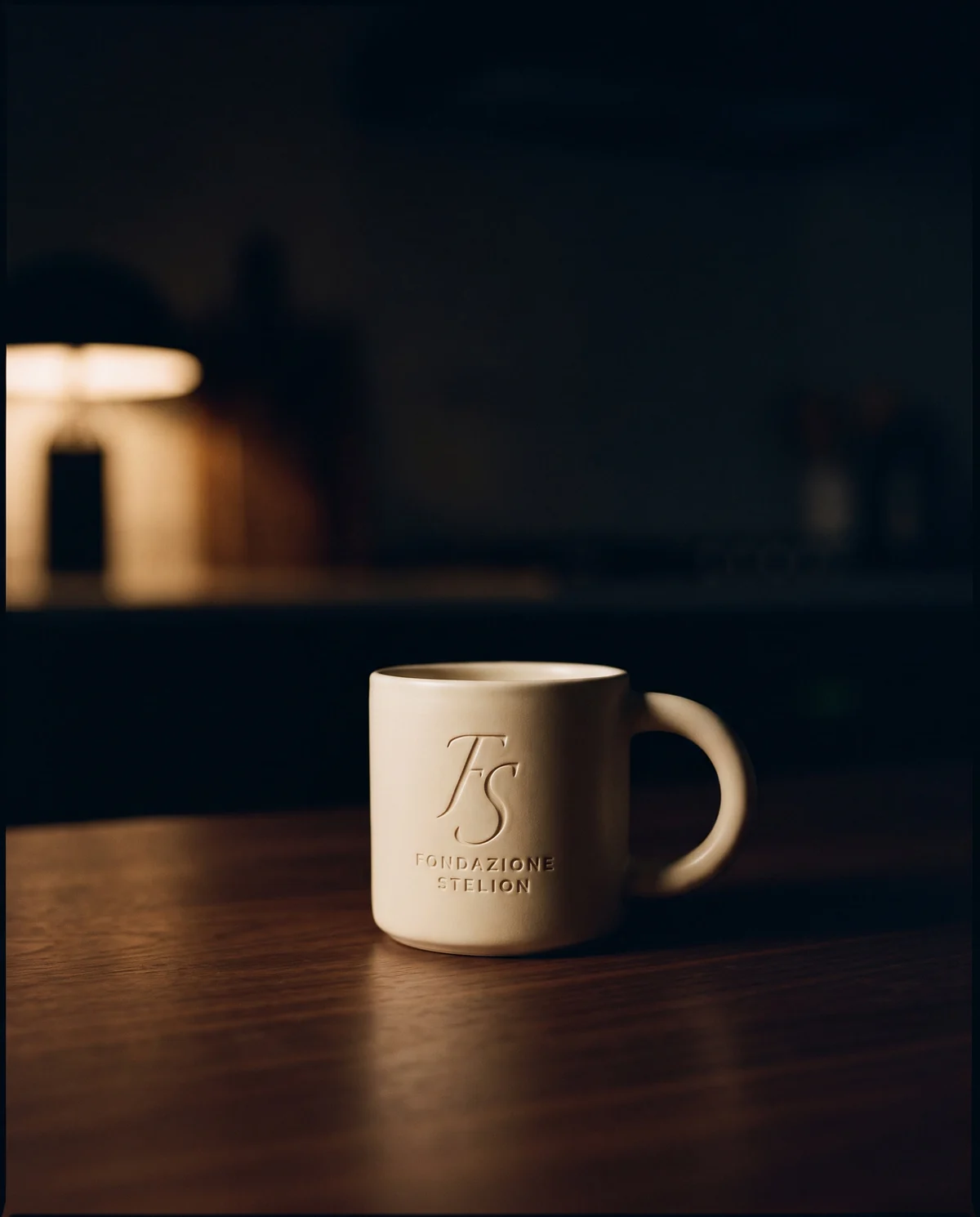 La tazza in gres a parete spessa, smalto opaco avorio, con il marchio inciso sul fianco.